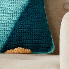 a crocheted pillow sitting on top of a couch next to a white chair