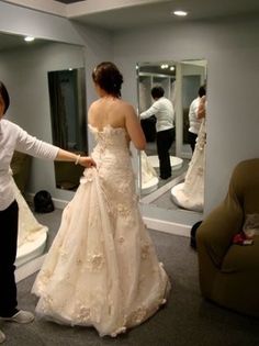 a woman in a wedding dress is looking at herself in the mirror while another man stands nearby