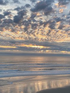 the sun is setting over the ocean with clouds reflected in the wet sand on the beach