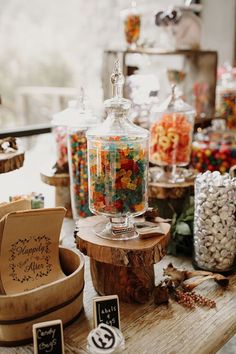 an assortment of candy and candies in glass jars on a table with wooden stand