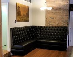 a black leather couch sitting on top of a hard wood floor next to a brick wall