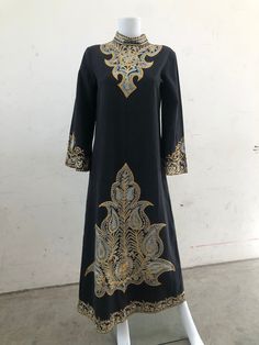 this unusually black 1970's embroidery kaftan is on a bee of Black cotton with gold lame embroidery. The back is fastened with hook and eyes and it has lovely 3/4 sleeves.  It has embroidery around the neck/ sleeves and hem. Around a size 10/ Small Traditional Long Sleeve Kurta For Evening, Gold Embroidered Dress For Eid, Traditional Embroidered Evening Dress, Traditional Embroidered Evening Kurta, Traditional Embroidered Dress For Evening, Traditional Embroidered Evening Dress With Intricate Embroidery, Traditional Embroidered Evening Dress With Intricate Details, Party Kaftan With Gold Embroidery For Festivals, Long Sleeve Kurta For Evening And Eid