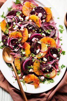 a white plate topped with beets and oranges next to a wooden spoon on top of a table