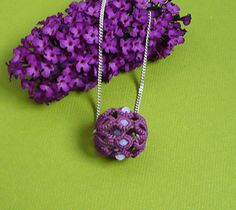 two necklaces made out of crochet are sitting next to purple flowers on a green surface