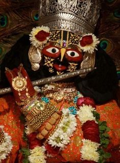 an elaborately decorated mask sitting on top of a colorful cloth covered floor next to flowers