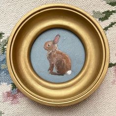 an image of a brown rabbit in a gold frame on a floral fabric tablecloth