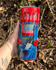 a hand holding up a red and blue can with scissors in it's pocket