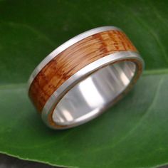 a wedding ring made out of wood and stainless steel on top of a green leaf