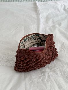 a crocheted purse sitting on top of a white bed next to a pillow