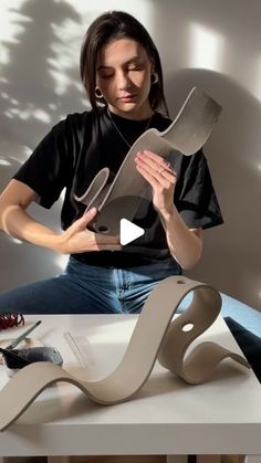 a woman sitting on top of a white table holding a piece of art with her hands