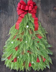 a christmas tree made out of green leaves and red ribbon on a wooden surface with white balls