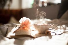 a steaming cup and book on a bed