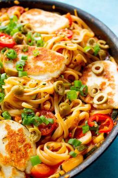 a skillet filled with pasta and vegetables on top of a blue countertop, ready to be eaten