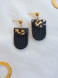 two pairs of black and gold earrings sitting on top of a white sheet