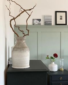 a white vase sitting on top of a table next to a black dresser with flowers in it