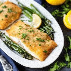 two fish fillets with asparagus on a plate next to lemon wedges