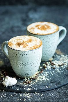 two coffee mugs sitting on top of a plate with whipped cream in the middle