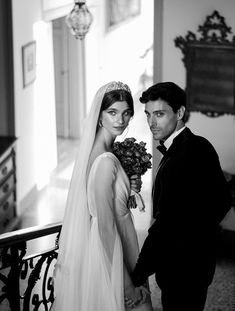 a man and woman standing next to each other in front of a stair case holding flowers