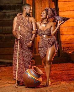 two african women dressed in traditional clothing standing next to a pot and holding a stick