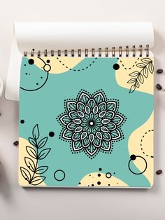 a spiral notebook with a flower design on it next to coffee beans and a cup of coffee