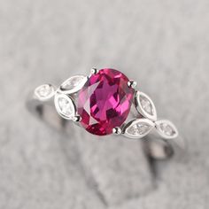 a ring with a pink stone and white stones on it's sides, sitting on top of a gray surface