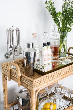 a wicker bar cart with bottles and glasses on it next to a vase filled with flowers