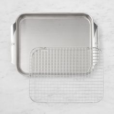 two stainless steel baking pans on a white marble counter top, one with a wire rack and the other without