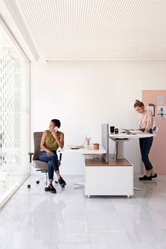 two women sitting at desks in an office with pink walls and white flooring