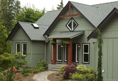 a green house with brown trim and red door, surrounded by greenery and trees