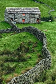 an old stone house in the middle of a green field with sheep grazing on it