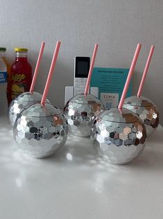 three shiny silver balls with pink straws in them on a white table next to some drinks