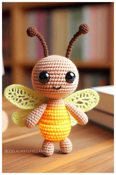 a small crocheted insect sitting on top of a wooden table next to a book