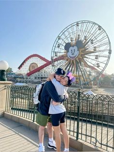 a man and woman hugging in front of a ferris wheel at an amusement park with mickey mouse on it