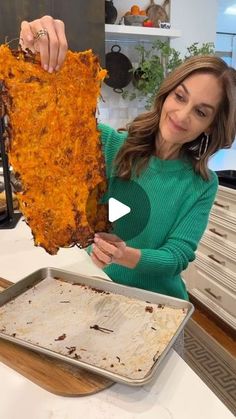 a woman holding up a large piece of food in front of a pan on a counter