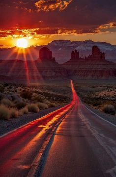 the sun is setting on an empty road in the middle of the desert with mountains behind it