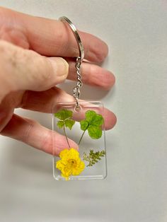 a hand holding a clear square keychain with yellow and green flowers in it