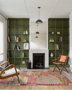 a living room with green bookshelves and two chairs in front of a fireplace