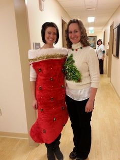 two women standing next to each other wearing christmas sweaters and holding decorations on their arms