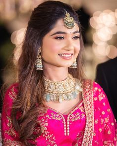 a woman wearing a pink and gold outfit with jewelry on her neck, smiling at the camera