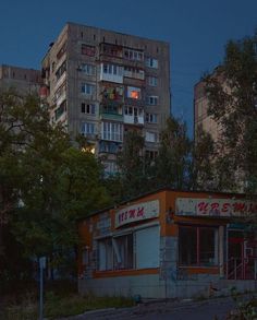 an old run down building in the middle of a city at night with buildings lit up behind it