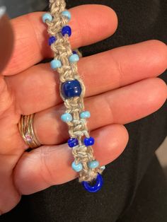 someone is holding a crocheted bracelet with blue beads and gold rings on their fingers