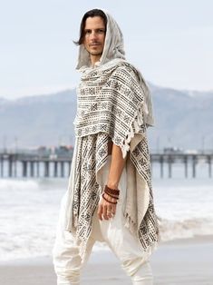 a man standing on top of a beach next to the ocean wearing a shawl