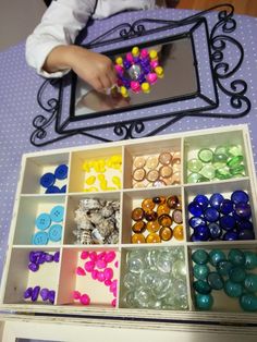 a child is playing with buttons in a box on the table next to a mirror