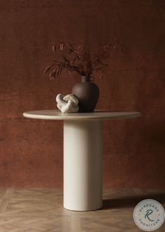 a vase with some flowers in it sitting on top of a white table next to a brown wall