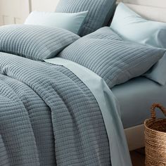 a bed with blue sheets and pillows on top of it next to a wicker basket