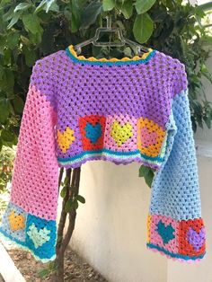 a colorful crocheted sweater hanging on a tree branch in front of a white wall