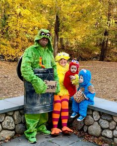 three children dressed as sesame characters posing for a photo in front of a barrel with a sign on it