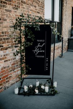 an outdoor ceremony with candles and greenery on the ground next to a brick wall