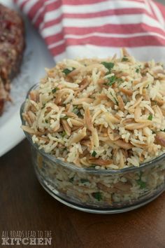 a glass bowl filled with rice on top of a wooden table next to some meat