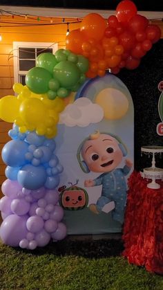 there are many balloons and decorations on the grass outside in front of a house that is decorated with an image of a baby's first birthday